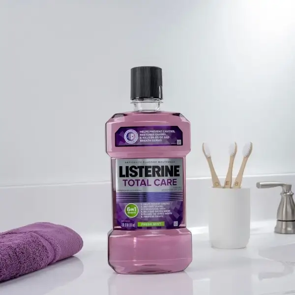 A purple Listerine Total Care bottle appears next to a faucet and sink. To its left a purple washcloth and to the right 3 wooden toothbrushes